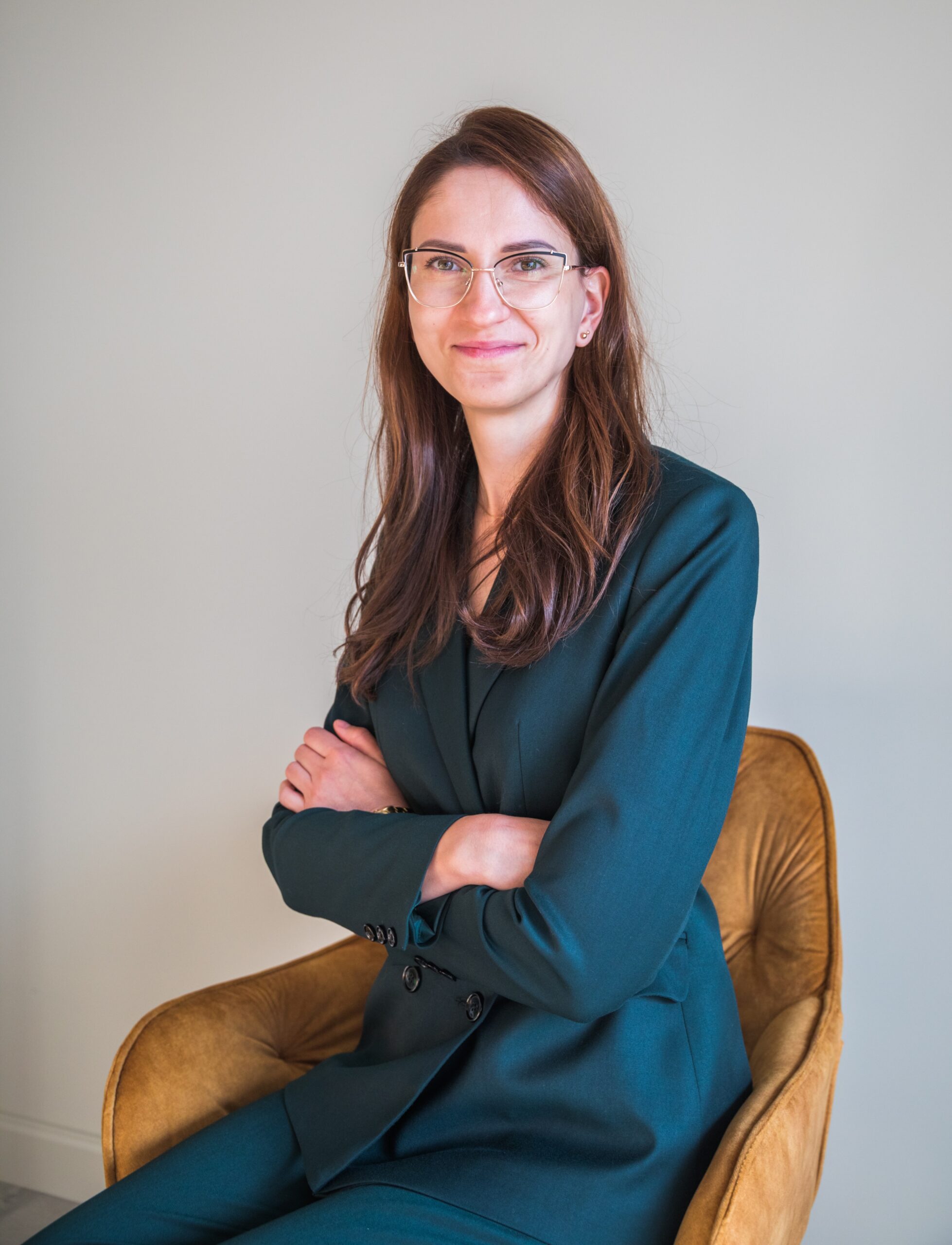 Ginekolog Kaja Majda. Jest ubrana w zielony garnitur. Siedzi na musztardowym krześle.